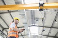 Low angle view of manual worker operating crane lifting steel in industry