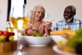 Low angle view of multiracial cheerful senior couple having lunch at dining table in nursing home Royalty Free Stock Photo