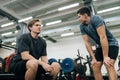 Low-angle view of of muscular personal instructor explaining technique of exercise to young beginner sportsman sitting Royalty Free Stock Photo