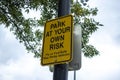 Low angle view of a Park At Your Own Risk sign outside of a baseball field, warning anyone parking their cars of the chance of fly