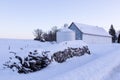 Low angle view of piles of cut wood and farm buildings covered in fresh snow during a blue hour winter morning Royalty Free Stock Photo