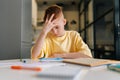 Low-angle view portrait of exhausted pupil boy tired from studying holding head head with hand sitting at desk with Royalty Free Stock Photo