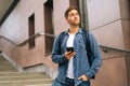 Low-angle view of portrait of handsome delivery man with thermo backpack holding using mobile phone standing on stairs Royalty Free Stock Photo