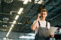 Low-angle view of professional handsome young mechanic male wearing uniform holding clipboard and talking on mobile Royalty Free Stock Photo