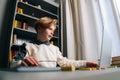 Low-angle view of pupil boy using typing laptop computer doing online lesson via Internet sitting at desk, selective Royalty Free Stock Photo