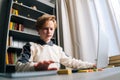 Low-angle view of pupil boy using typing laptop doing online lesson via Internet at desk, selective focus. Royalty Free Stock Photo