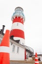 A low angle view of a red and white striped lighthouse with a ladder curling up towards it. A building red and white cone is on