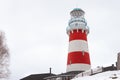 A low angle view of a red and white striped lighthouse with white wooden fence leading to it. A house is on the bottom of the Royalty Free Stock Photo