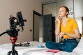 Low-angle view of redhaired female beauty blogger making video tutorial using professional camera standing on tripod Royalty Free Stock Photo