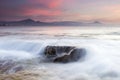 Low angle view of the sea, a small waterfall, mountains, and mesmerizing clouds during sunset Royalty Free Stock Photo