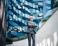 Confident elderly entrepreneur standing with arms crossed against modern office buildings Royalty Free Stock Photo