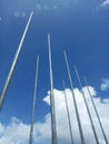 Low angle view of several tall silver flagpoles against a clear blue sky with white clouds. Royalty Free Stock Photo