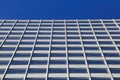 Low angle view on skyscraper facade with geometric symmetrical pattern lines against deep blue cloudless sky