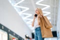 Low-angle view of smiling attractive blonde young woman in stylish clothing talking on mobile phone, holding shopping Royalty Free Stock Photo