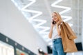 Low-angle view of smiling attractive blonde young woman talking on mobile phone looking at camera, holding shopping Royalty Free Stock Photo