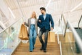 Low-angle view of smiling beautiful young couple holding shopping paper bags with purchases and walking down stairs Royalty Free Stock Photo