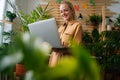 Low-angle view of smiling young business woman floral store owner standing with laptop holding in hand among green Royalty Free Stock Photo