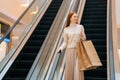 Low-angle view of smiling young woman holding on escalator handrail and riding escalator going up in shopping mall Royalty Free Stock Photo