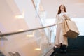 Low-angle view of smiling redhead young woman shopper holding on escalator handrail and riding escalator going down in Royalty Free Stock Photo