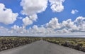 Low angle view of straight road through scenic volcanic landscape against blue sky and white clouds, Lanzarote