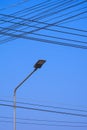 Street light post with busy electric power lines against blue sky background in vertical frame Royalty Free Stock Photo