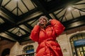 Low-angle view of stylish portrait of cheerful redhead young woman in warm winter clothes talking using holding mobile Royalty Free Stock Photo