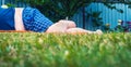 Low-Angle View of Unrecognizable Barefoot Big Fat Man in Blue Shirt and Plaid Shorts Lying on Mowed Green Grass Lawn with Blurred