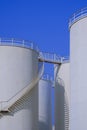 White fuel storage tanks with spiral staircase against blue clear sky background in vertical frame Royalty Free Stock Photo