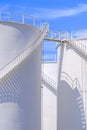 Low angle view of white fuel tanks with spiral staircase against blue sky background Royalty Free Stock Photo