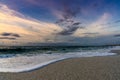 Low angle view of white sand beach with waves rolling in under a colorful sunset sky Royalty Free Stock Photo
