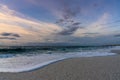 Low angle view of white sand beach with waves rolling in under a colorful sunset sky Royalty Free Stock Photo