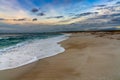 Low angle view of white sand beach with waves rolling in under a colorful sunset sky Royalty Free Stock Photo