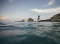 Rear view of woman paddling SUP board through passage between rocks Royalty Free Stock Photo