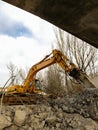 Low angle view of a yellow excavator running a reinforced concrete demolition with a hydraulic breaker