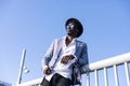 Low angle view of a young african black man wearing hat and sunglasses leaning on a metallic fence relaxing while looking away in Royalty Free Stock Photo