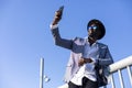 Low angle view of young african black man wearing hat and sunglasses leaning on a metallic fence relaxing while taking a selfie in Royalty Free Stock Photo