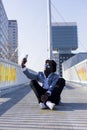 Low angle view of a young african black man wearing hat and sunglasses sitting on ground relaxing while taking a selfie in a sunny Royalty Free Stock Photo