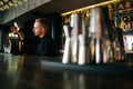 Low-angle view of young barman preparing refreshing alcoholic cocktail standing behind bar counter in modern dark