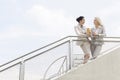Low angle view of young businesswomen talking while standing by railing against sky Royalty Free Stock Photo