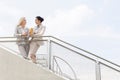 Low angle view of young businesswomen talking while standing by railing against sky Royalty Free Stock Photo