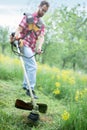 Low angle view of a young man mowing grass in orchard using a string trimmer Royalty Free Stock Photo