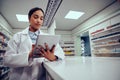 Low angle view of young female woman wearing labcoat working in chemist using digital tablet to confirm online order Royalty Free Stock Photo