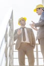 Low angle view of young male businessmen in hard hats having discussion on stairway against clear sky