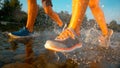 LOW ANGLE: Young athletic couple running in shallow river water on sunny day.