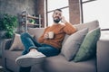 Low below angle view portrait of his he nice attractive cheerful cheery bearded guy sitting on divan drinking latte