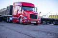 Low cab bright red big rig semi truck with loaded flat bed semi trailer standing on the parking lot in row with another semi Royalty Free Stock Photo