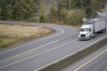 Low cab profile big rig semi truck transporting cargo in covered bulk semi trailer driving on the divided highway road with fork