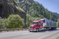 Low cab profile bright red big rig semi truck transporting cargo in covered framed semi trailer moving on the wide highway road Royalty Free Stock Photo