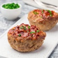 Low carb paleo meat cups, stuffed with champignons, bacon and cheese, garnished with green onion, on white plate, square format