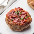 Low carb paleo meat cups, stuffed with champignons, bacon and cheese, garnished with green onion, on white plate, square format,